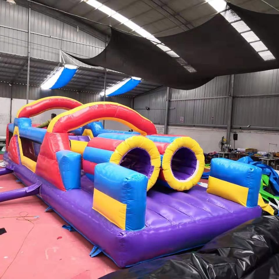 Red, blue, and yellow inflatable obstacle course with tunnel entries, set up indoors